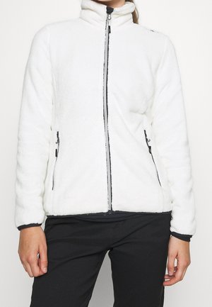 Personne portant une polaire blanche zippée avec une fermeture éclair noire et deux poches latérales zippées, associée à un pantalon noir.