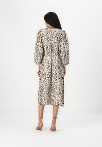 Midi-mekko, jossa on leopardikuosi beige- ja mustavalkoisena, puffihihat, vyötäröä korostava malli ja laskeutuva helma. Yhdistetty nyöritettävien kenkien kanssa.