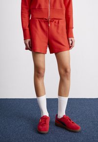 Shorts de sport rouges avec taille à cordon, associés à des baskets rouges et des chaussettes blanches jusqu'à la cheville. Le tissu présente un motif texturé.
