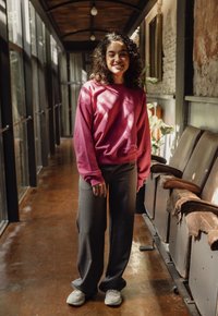 Roze sweatshirt, donkergrijze broek en witte sneakers. De outfit heeft een ontspannen pasvorm en is gemaakt van zachte, textuurvolle materialen.