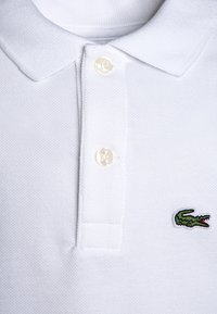 Polo shirt in cotone bianco con finitura testurizzata, colletto classico e due bottoni. Presenta un logo di coccodrillo ricamato verde sul petto.