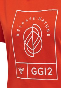 Pomarańczowa koszulka z białym geometrycznym wzorem liścia, powyżej zaokrąglony tekst „RELEASE NATURE”, ikona pszczoły oraz „GG12” w ramce graficznej.