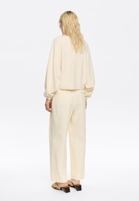 Maglione color crema, morbido al tatto, con maniche a palloncino e vestibilità comoda, abbinato a pantaloni leggeri a vita alta e gamba dritta dello stesso colore.