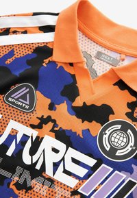 Oranž ja must kamuflaažiga spordipaita, millel on krae, valged triibud ja logo plaastrid. Valmistatud hingavast võrgusilma materjalist.
