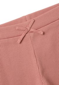 Lichtroze ribbelstof van broeken met een elastische tailleband en een strikdetail. Close-up toont textuur en stiksel.