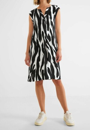 Vestido sin mangas en blanco y negro con cuello en V, que presenta un audaz estampado de cebra y una forma relajada en línea A. Combinado con zapatillas blancas.