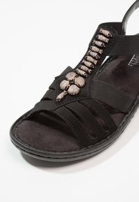 Czarne sandały o teksturowanym pasku, ozdobione metalicznymi akcentami w kształcie kwiatów oraz miękkim wyściółką zapewniającą komfort.