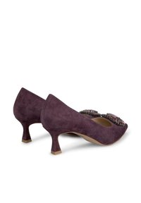 Tacchi in suede viola con un tacco basso e scolpito. Presentano decorazioni nell'area delle punte, che aggiungono texture e interesse visivo.
