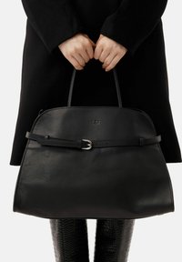 Czarna skórzana torebka o konstrukcji z płaską podstawą, dwoma górnymi uchwytami i ozdobą w formie paska. Na przodzie znajduje się subtelne tłoczone logo.
