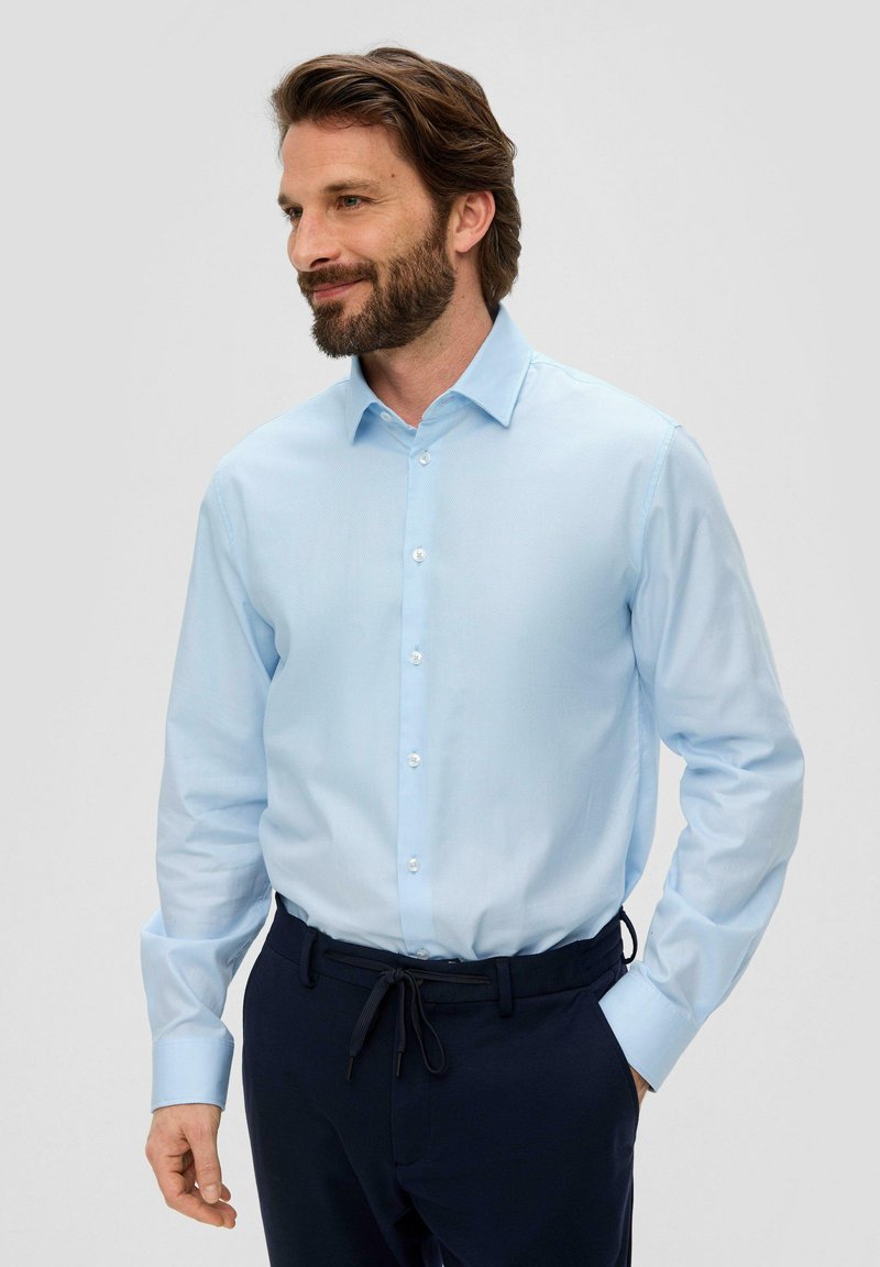 Chemise à manches longues bleu clair avec un devant à boutons et un col pointu, fabriquée dans un tissu lisse ; associée à un pantalon marine doté d'une taille élastique.