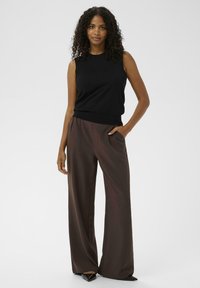 Zwarte mouwloze top gecombineerd met hoge taille, wijde bruine broek. De broek heeft een gladde textuur, met zijzakken en een relaxte pasvorm.