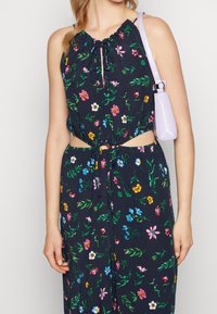 Blommönstrad crop top i mörk marinblå, med dragsko vid halsringningen och utskärningar på sidorna. Matchad med en liten, ljuslila handväska.