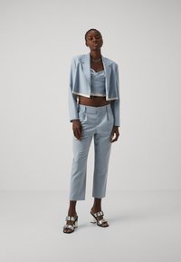 Világoskék crop blézer egy azonos színű crop toppal, elegáns nadrágokkal párosítva. Ezüst csatos szandálok teszik teljessé az öltözéket.