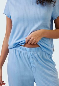 Ljusblå bomullspyjamas i ribbad struktur. T-shirten har korta ärmar och byxorna har resårmidja och knappdetalj.