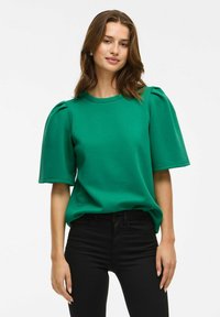 Sudadera verde con mangas cortas abombadas, escote redondo y textura suave, combinada con pantalones negros ajustados.