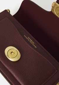 Dark burgundy leather purse with gold clasp and text inside reading "THE TABBY BAG GENUINE FULL GRAIN LEATHER."