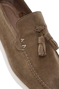 Mocasines de ante marrón con borlas de cuero, que presentan detalles de costura y una suela de goma blanca. Textura suave y diseño redondeado.