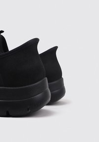 Chaussures de sport noires avec une tige en daim doux et une semelle en caoutchouc. Présente un dos arrondi et une semelle texturée pour une meilleure adhérence. Design simple et moderne.