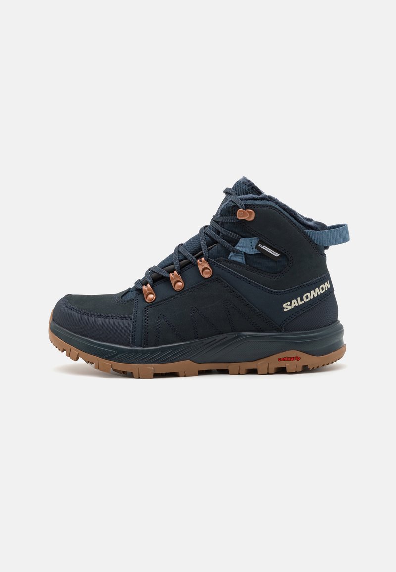 Donkerblauwe mid-top wandelschoen gemaakt van synthetische materialen, met bruine accenten, gestructureerde panelen en een rubberen buitenzool met grip.