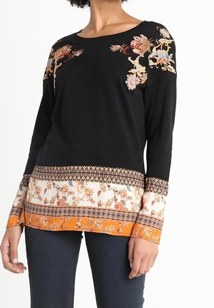 Pull noir à manches longues avec broderie florale sur les épaules et ourlet à motifs multicolores, porté avec un jean foncé.