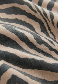 Beige stof met een zwart zebra-printpatroon, met zichtbare plooien en textuur van het gewoven materiaal.