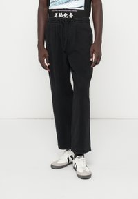 Svarta, löst sittande byxor med elastisk midja, med en slät yta. I kombination med vita och grå sneakers.