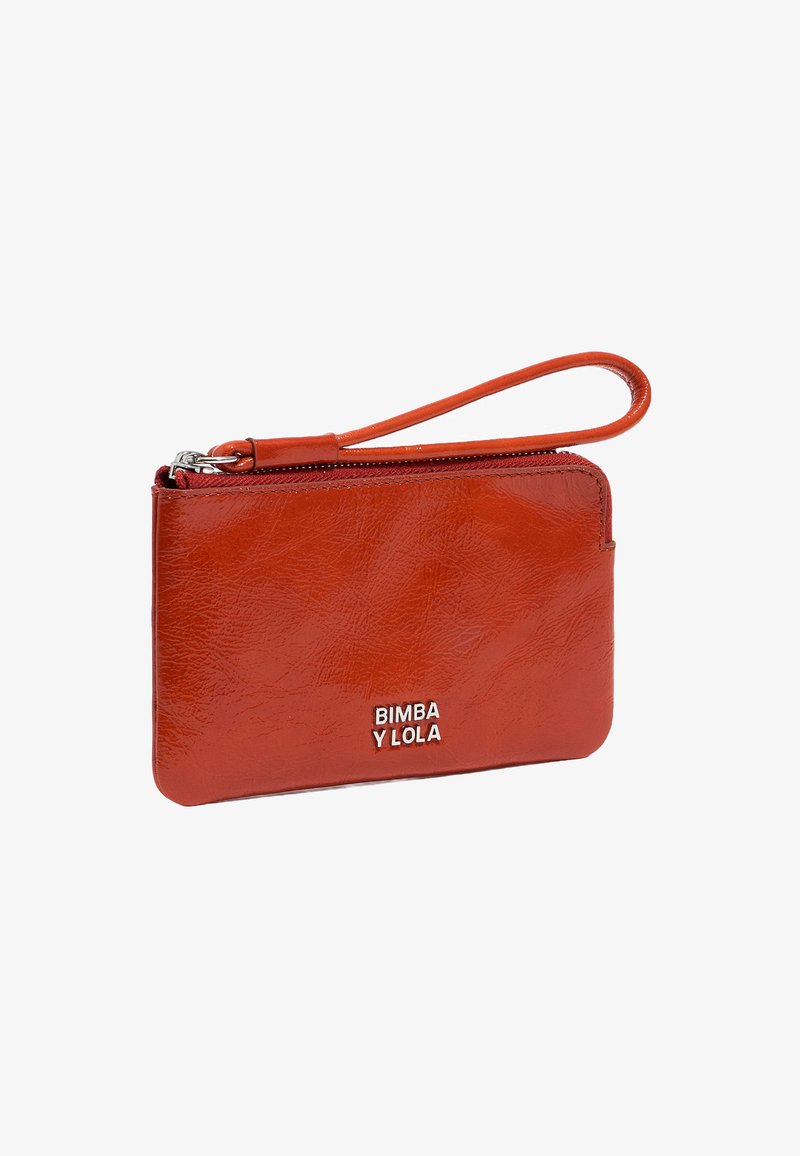 Cartera de imitación de cuero roja con cierre de cremallera y correa para la muñeca. Presenta un logotipo en letras plateadas en la parte frontal. Textura suave, forma rectangular.