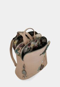 Zaino in pelle beige con più scomparti aperti che mostrano un rivestimento in tessuto colorato a motivo, spallacci regolabili e cursori in metallo per la cerniera.