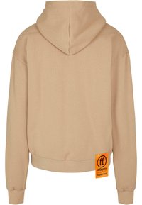 Beige kapucnis pulóver laza szabással, bordás mandzsettával és szegéllyel; oldalán fekete feliratos narancssárga címke található. Puha szövettextúra.