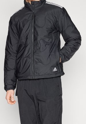 Giacca nera isolata con texture trapuntata, colletto alto, zip completa e tre righe bianche sulle spalle. Presenta il logo Adidas sull'orlo.