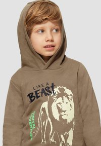 Braun Hoodie aus Baumwollmischung. Mit einem Löwengrafik und dem Text "WIE EIN BESTIE" in Schwarz, dazu "DIGITALE ABENTEUER" in Grün.