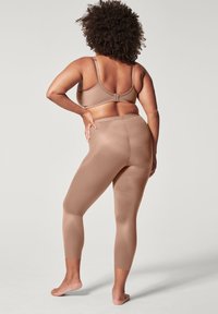 Beige sports-bh og matchende tights, tettsittende design, jevn tekstur, lett materiale, mid-rise tights som slutter rett ovenfor ankelen.
