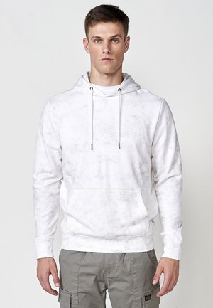 Witte katoenen hoodie met een zachte textuur, voorzien van een voorkantzak, trekkoorden en een subtiel patroon. Gecombineerd met grijze cargo pants.