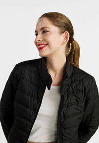 Czarna pikowana kurtka z wysokim kołnierzem i zapięciem na zamek błyskawiczny. Lekki materiał ma subtelne detale przeszycia. Nosić ją na białej bluzce.