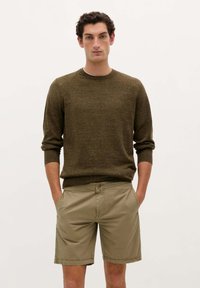 Pulover tricotat maro cu guler rotund și manșete cu dantelă, asortat cu pantaloni scurți khaki cu buzunare laterale și închidere cu nasture.