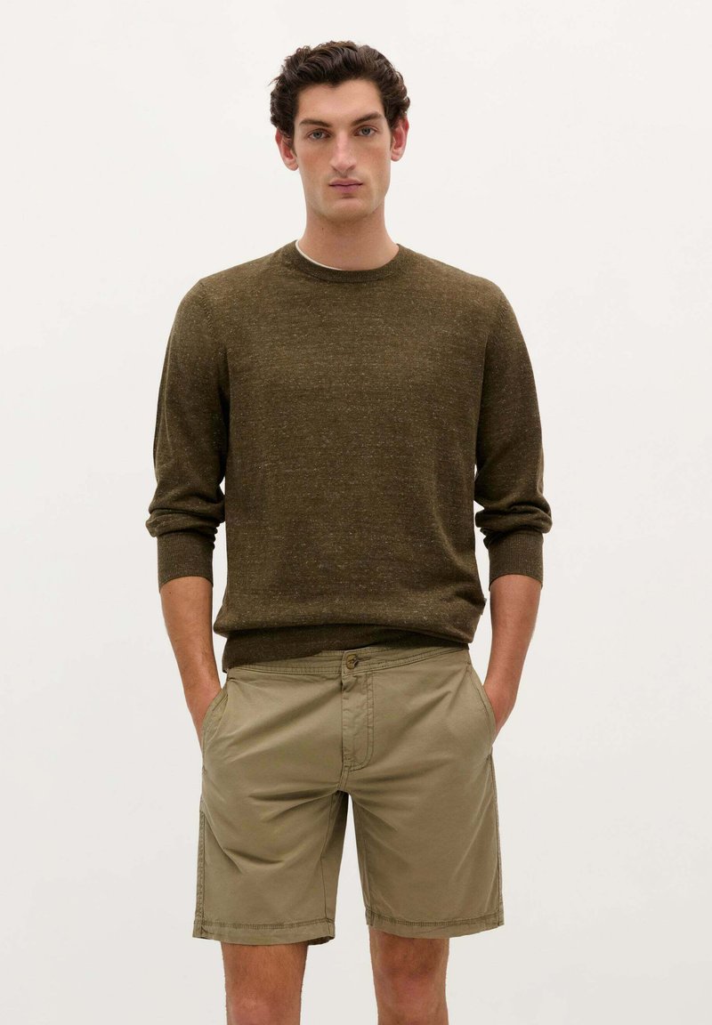 Pull en maille marron à col rond et poignets côtelés, associé à un short kaki avec poches latérales et fermeture à bouton.