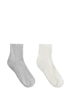 Para skarpetek do kostki, jedna szara z antypoślizgowymi kropkami na podeszwie, druga gładka biała, obie prążkowane i wykonane z miękkiej tkaniny.