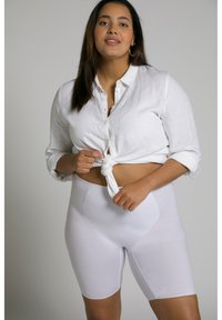 Camicia bianca di lino annodata in vita, abbinata a pantaloni corti bianchi, morbidi e aderenti. Design semplice, lieve lucentezza e senza motivi visibili.