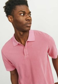 Roza polo majica iz bombaža, z dvema gumboma na zapiranju ter majhnim vezenim logotipom na prsih. Kratki rokavi in klasičen ovratnik.