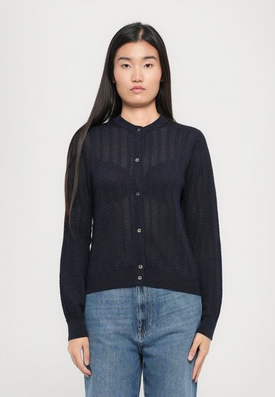 Jūras spēku zilas adītas kardigānas ar strukturētu rakstu, pogu priekšpusi un ribotām piedurknēm. Saskanīgas ar gaiši ziliem brīvi pieguļošiem džinsiem.