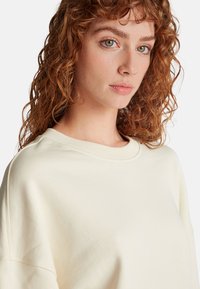 Felpa color crema con collo a girocollo a coste e texture morbida, caratterizzata da cuciture delle spalle scese per una vestibilità comoda.