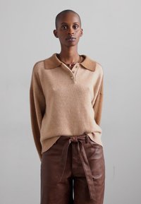 Light brown knitted sweater with a collared neckline and three-button placket, paired with textured brown leather pants featuring a tie waist.