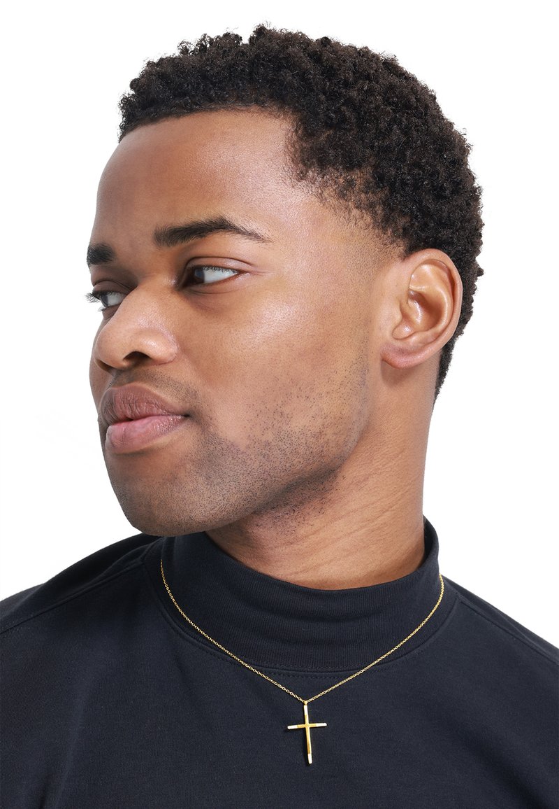 Goldene Kreuzkette mit einer dünnen Kette, getragen über einem schwarzen Rollkragenpullover, mit glatter metallischer Textur und minimalistischem Design.