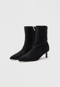Stivali ankle in suede nero con punta affusolata, tacco di altezza media e chiusura con zip laterale. Texture liscia con un design elegante e minimalista.