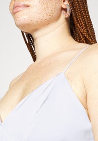 Vestido de cetim cinza claro com alças finas e decote drapeado. Apresenta pele texturizada com sardas e cabelo intrincadamente trançado.