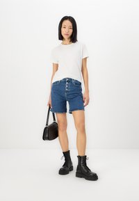 Hvit t-skjorte med rund hals, høy-midje blå denimshorts med fem knapper og to lommer, svarte militærstøvler, bærende en svart håndveske.