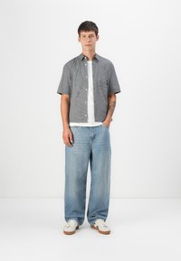 Short-sleeve, black and white checkered shirt with a front pocket, paired with light blue wide-leg jeans and white sneakers.