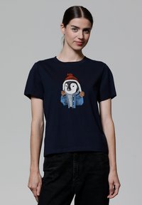 Navyblauwe katoenen t-shirt met een geborduurde pinguïn in een rode hoed en spijkerjack, met bruine pompons op de capuchon van de jas.