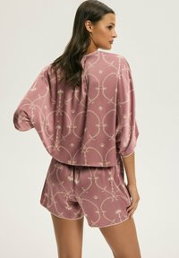 Krótki rękaw, przycięta bluzka i pasujące szorty w miękkim różowym satynie z subtelnym złotym wzorem geometrycznym i luźnym krojem.