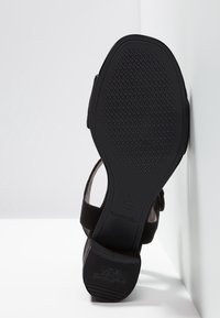 Sandale en suede noir avec une semelle en caoutchouc texturé, présentant un design de sangle simple. Taille 37 indiquée sur la semelle.